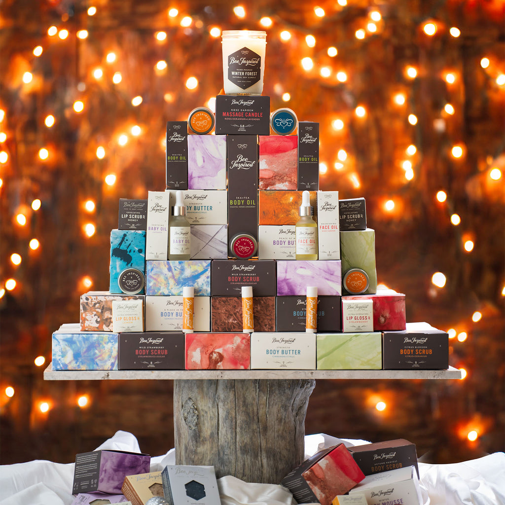 Bee Inspired Products stacked up to resemble a Christmas tree with soft yellow lights in the background