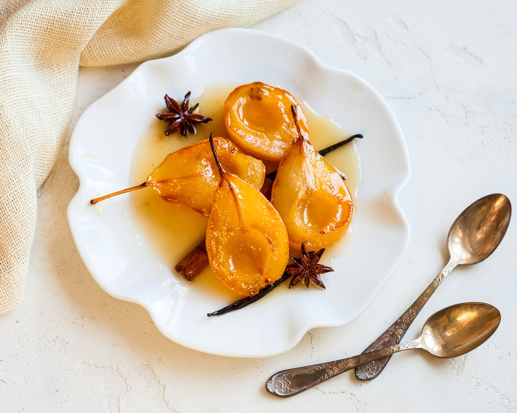 Poached Pears by Bee Inspired on a white dining plate next to two spoons