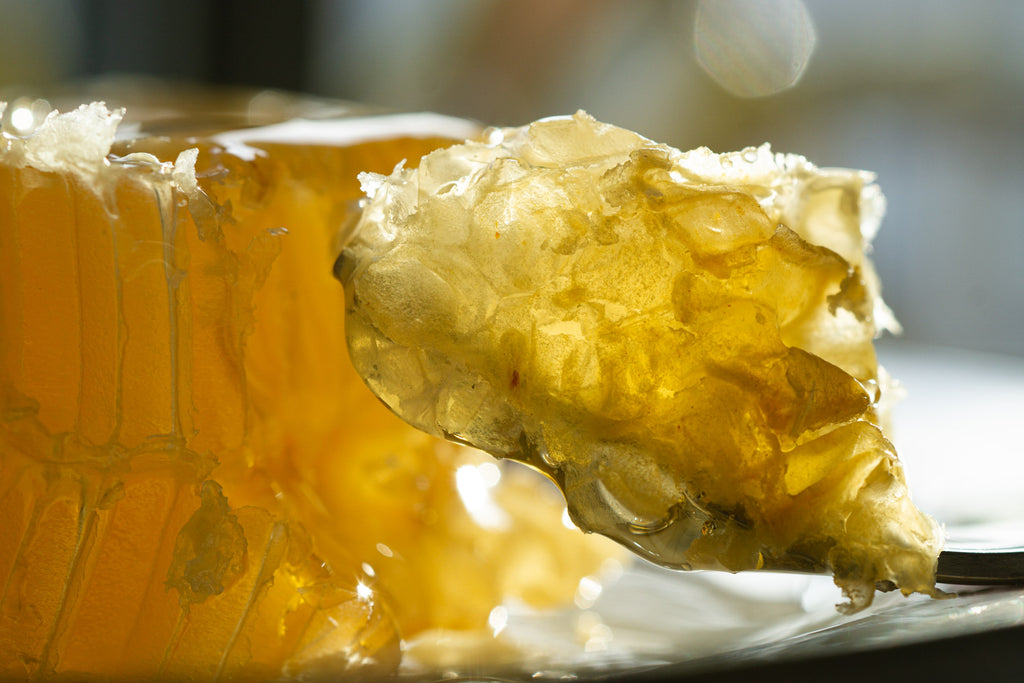 A piece of raw honeycomb on a fork in front of a block of raw honeycomb.