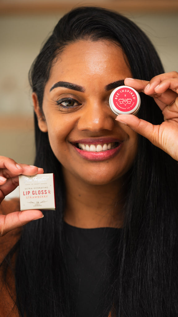 A woman holding our strawberry lip gloss in front of her eye