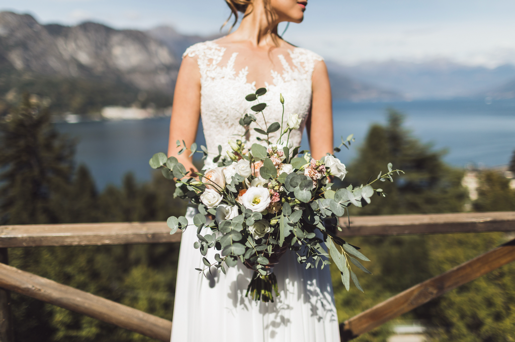 A bride holding a bouquet of white flowers in front of a scenic river through a mountain view