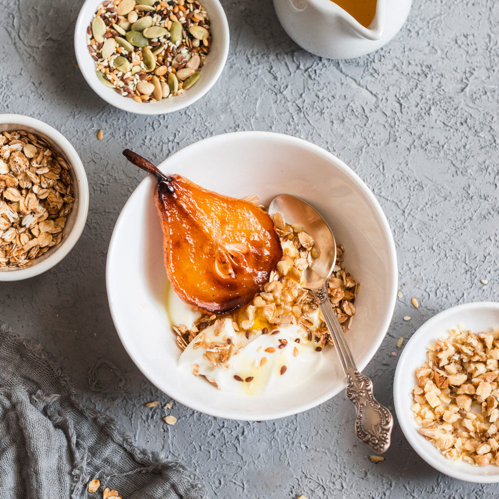 Caramelized Pear by Bee Inspired sitting in a white bowl with yogurt, granola, and a spoon