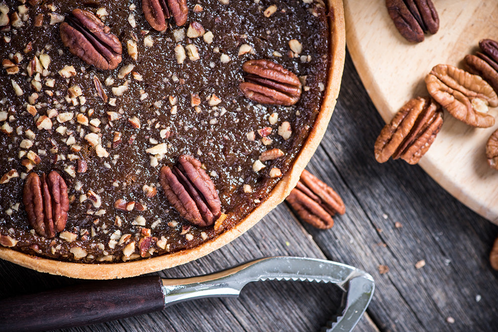 A Honey Pecan Pie on a table next to raw pecans and a pie cutter.