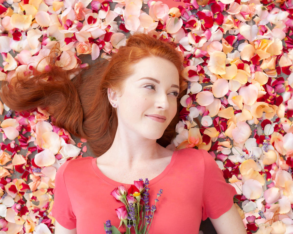 Woman laying down in a pile of rose petals holding flowers