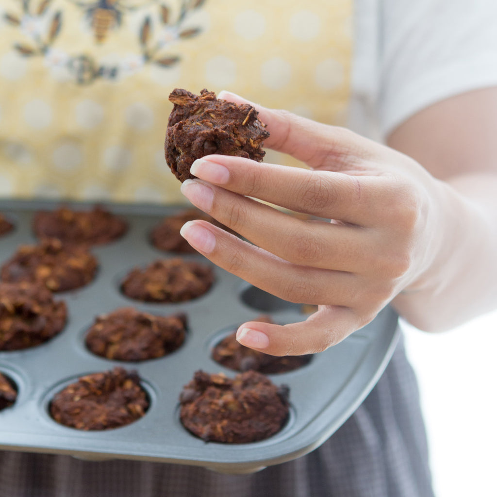 Female wearing a baking apron and holding a tray of muffins