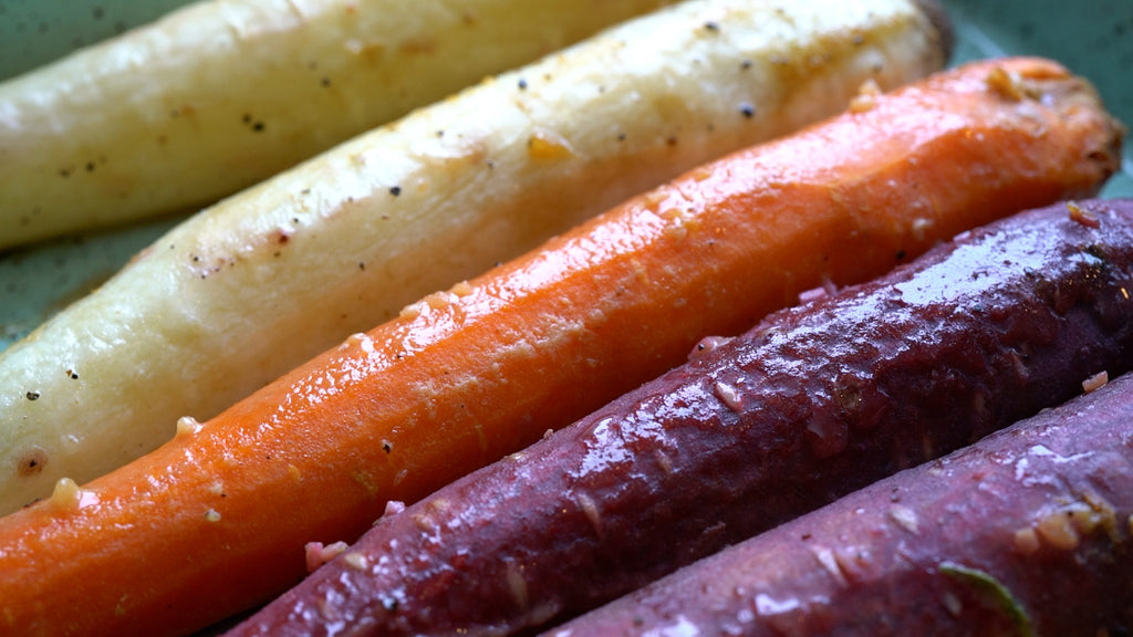 Purple, orange, and white carrots lined on a tray in marinade