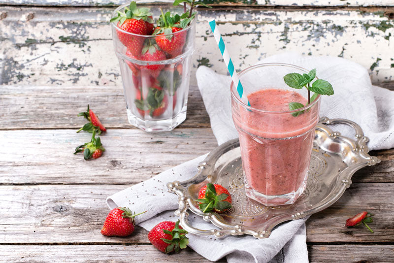 Strawberry smoothie on a table in front of a glass filled with strawberries