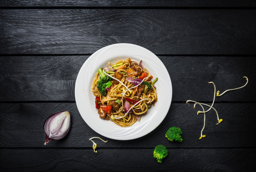 Asian Noodle Salad on black table with fresh vegetables surrounded by raw ingredients
