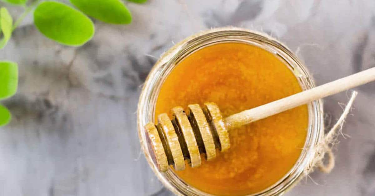 DIY Honey Body Scrub on marble table in package with part of a plant ready to use