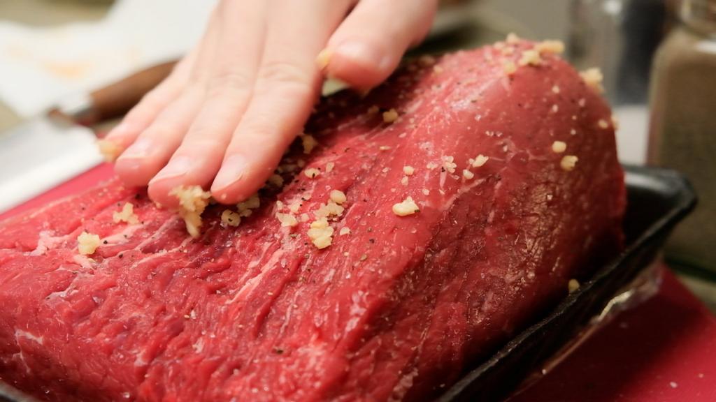 rubbing raw pot roast with hands covering with garlic and salt and pepper