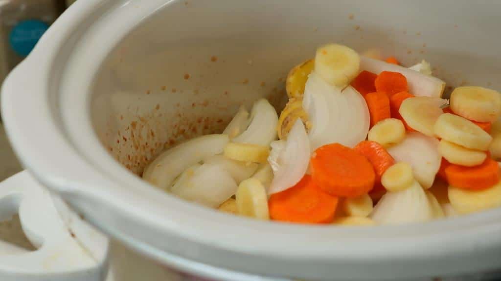 crockpot filled with herbs, spices, onion, carrots and parsnips