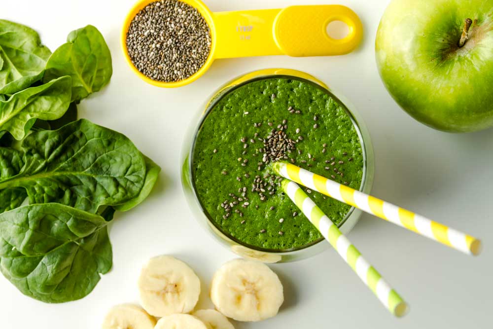 Bee Green Smoothies with straws with chia seeds and raw spinach, sliced banana and green apple