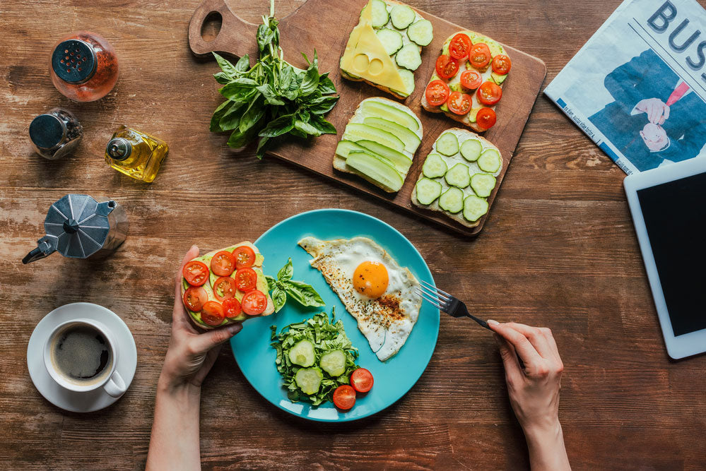 A very large Breakfast table shot overhead with 4 types of toast eggwhites on blue plate and arms ready to start eating in honor of Better Breakfast Month including newspaper