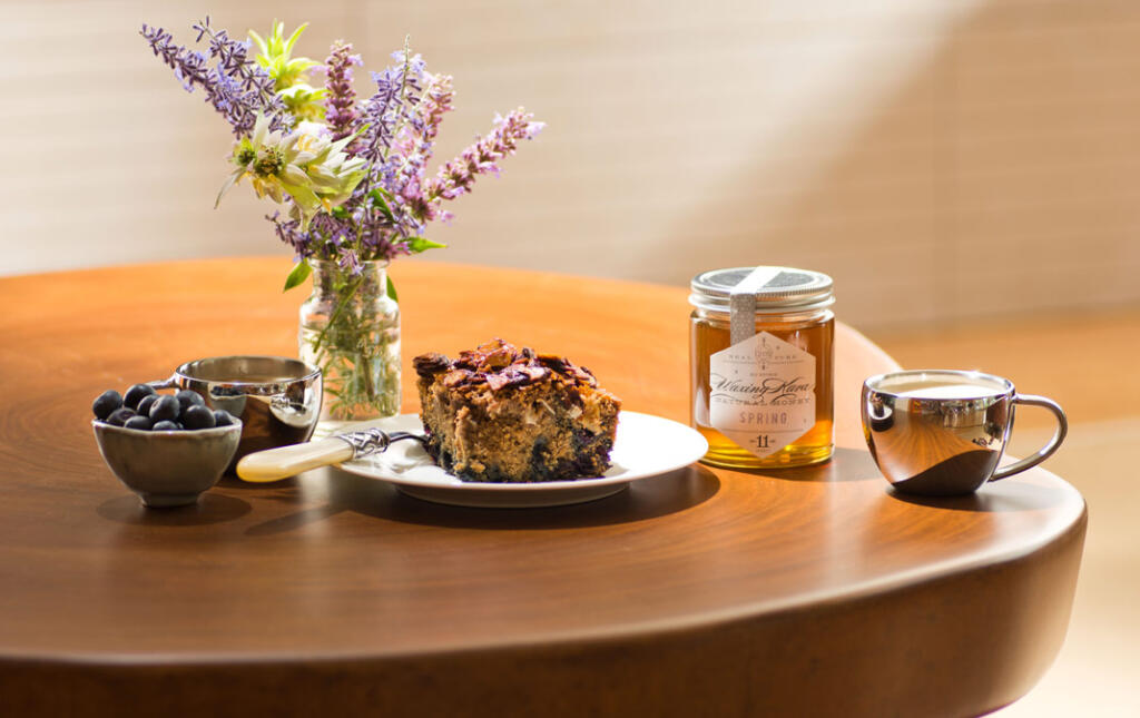 Healthy coffee cake set with honey, espresso and fresh picked wildflowers with bowl of fresh blueberries on wood stump table