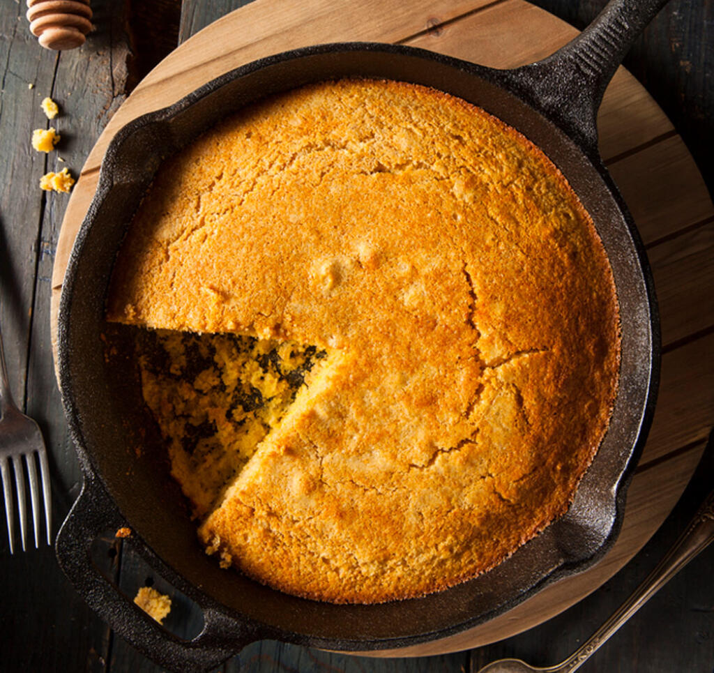 Cornbread in a round pan with a pie-shaped slice out of it still in skillet. Perfect for Thanksgiving Feast!