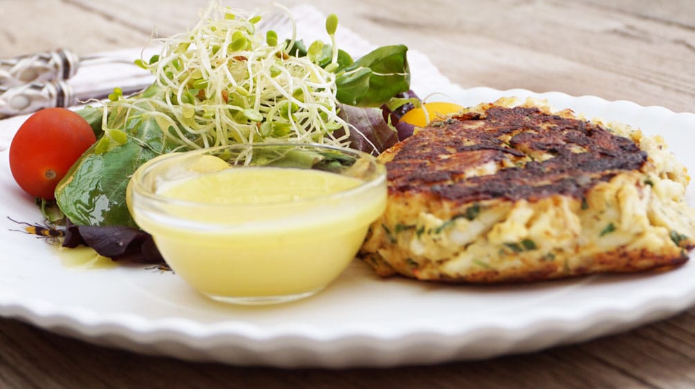 maryland crab cakes prepared and cooked on plate with dipping sauce next to green salad