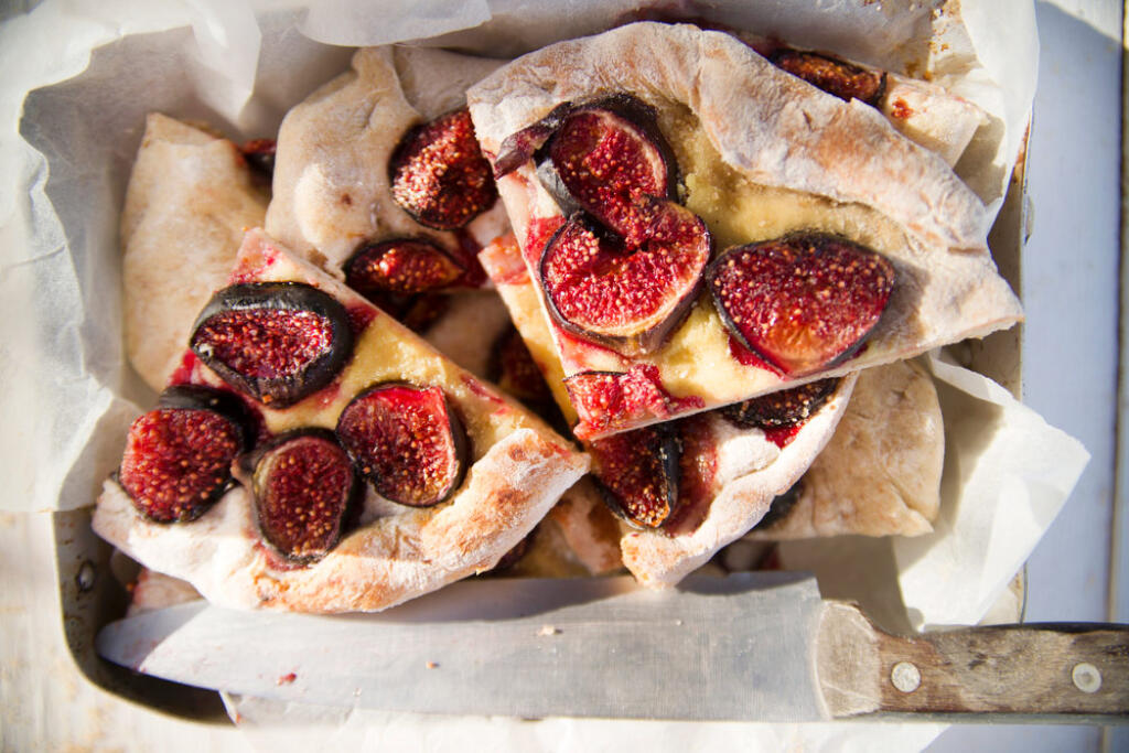 Fig Focaccia cut into pieces on parchment with knife on baking tray