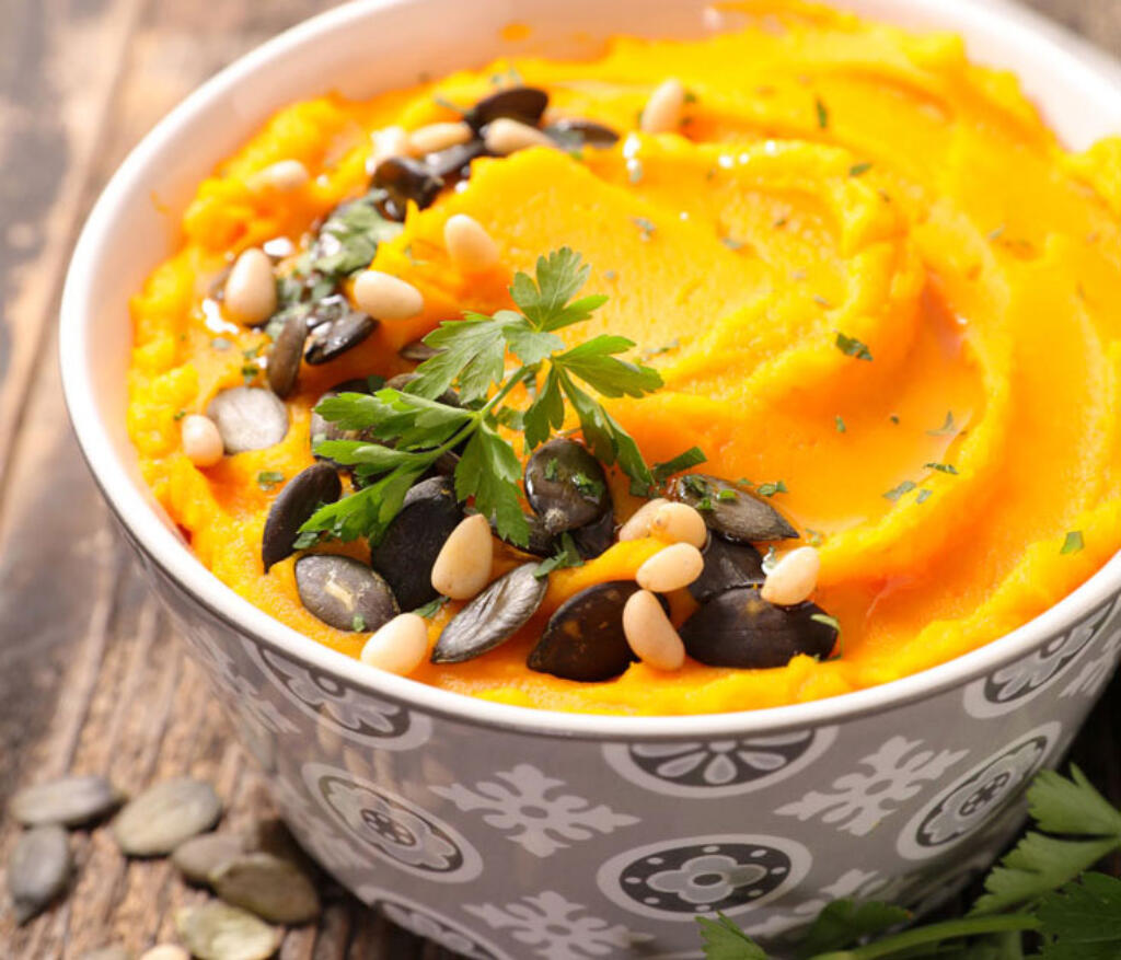 healthy mashed sweet potatoes with pine nuts and craisins and herb garnish on wood table