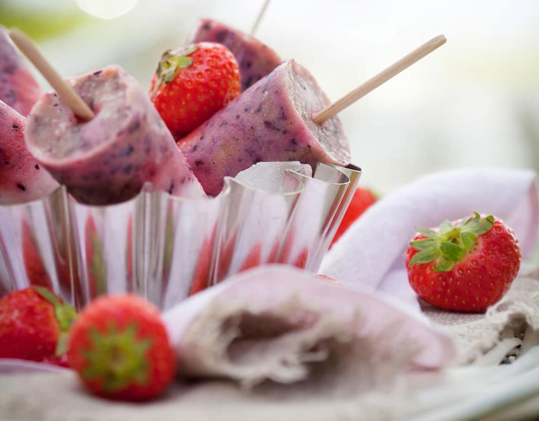 homemade berry popsicles in paper cup with fresh berries on table with napkin