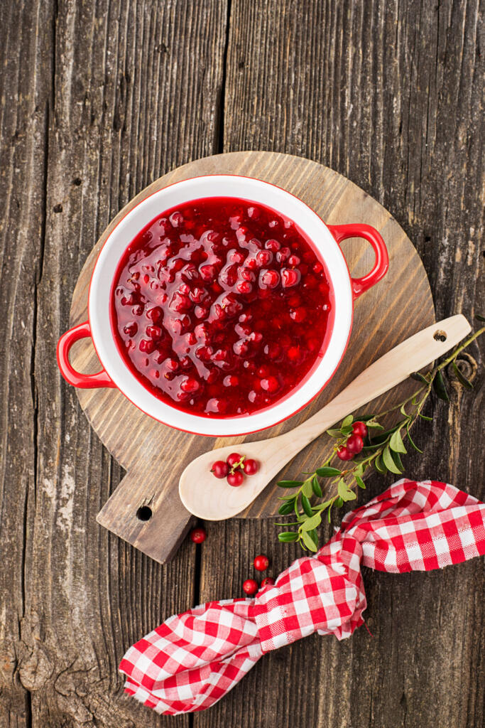 Honey Cranberry relish on cutting board on wood talbe with red gingham napkin and wooden serving spoon with cranberry garnish and sprig of holly