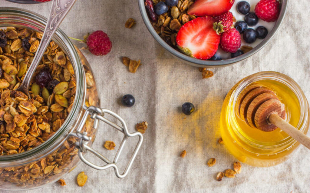 honey nut granola on table with fresh fruit and raw honey on linen tablecloth
