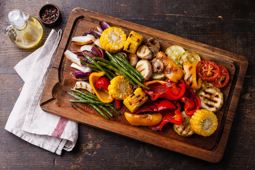 Summer Grilling Vegetables on a wood platter with a napkin and olive oil, in time for National Vegetarian Month