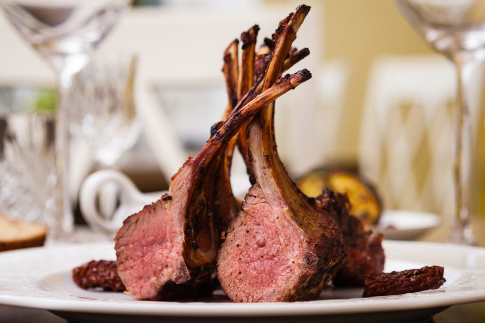 Honey Glazed Oven Roasted Lamb Chops plated on dining table surrounded by wine goblets
