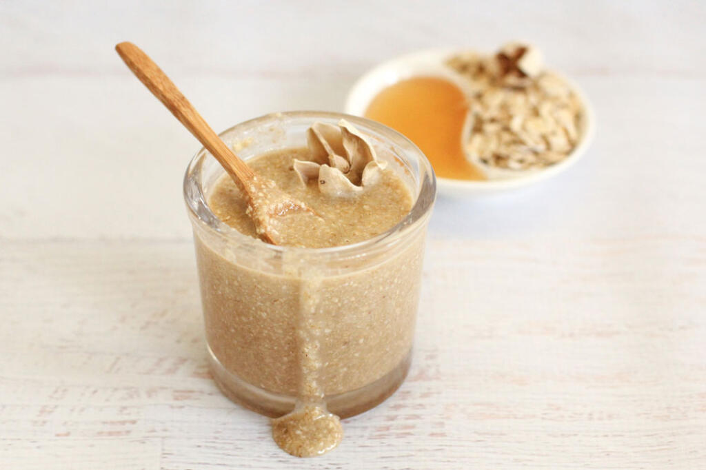 DIY Honey Oat Scrub in honor of National Oat Month, in glass with spoon with side-dish of honey