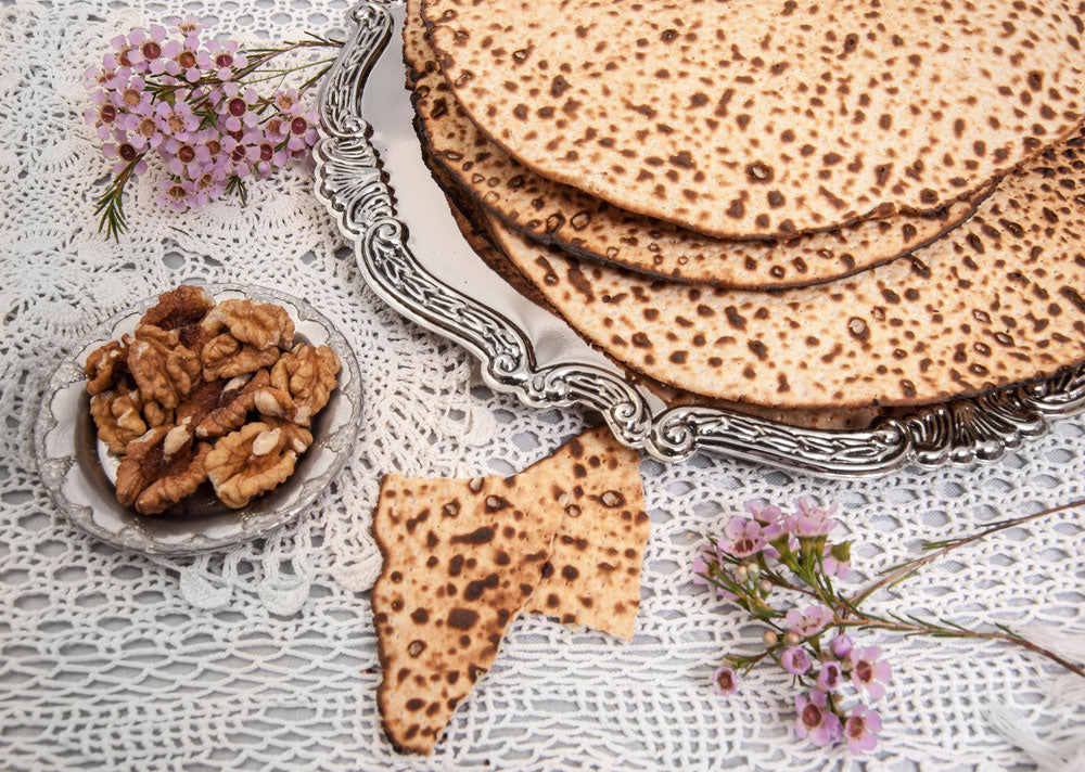 Passover Table with handmade Matzah and silver platter on white tablecloth and flowers and walnuts for making charoset