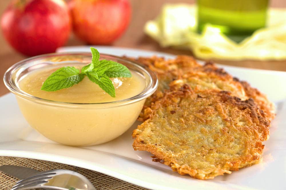 potato latkes and honey apple sauce on a white plate surrounded by ingredients to make them