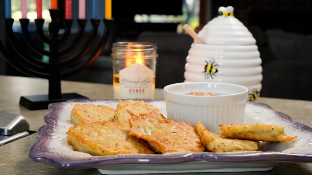platter of potatoe latkes with apple sauce honey and menorah on counter