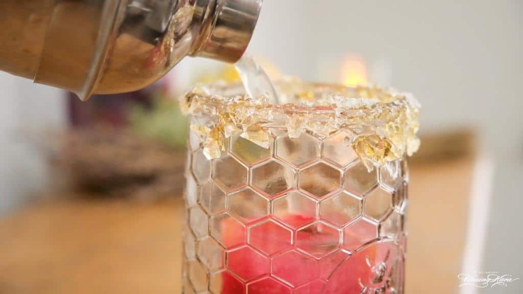 Pouring a Lemon Vodka Cocktail with honey lollipop rim from cocktail shaker