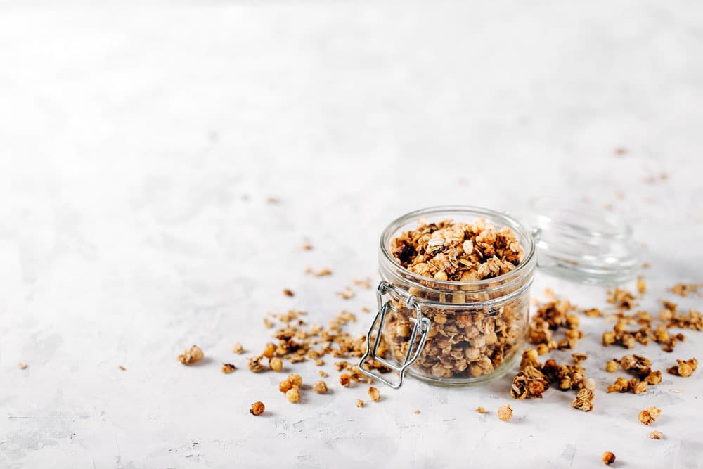 Raw honey nut granola in bale jar, lid open on grey fabric