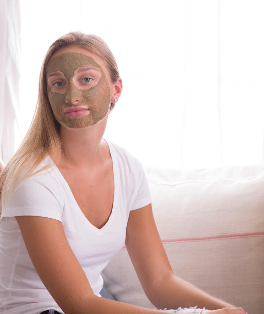 Beautiful girl with sea+tea mask on her face in front of a window