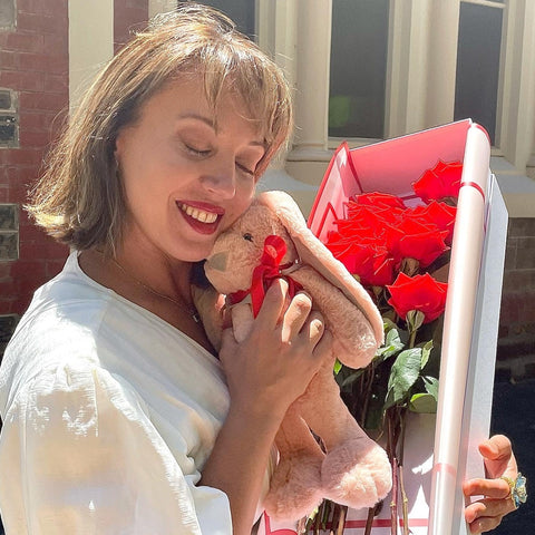 A gentle embrace with the soft plush bunny nestled against Floral Atelier Australia's Dozen Ferrari Red Roses, a picture of serenity and affection in Adelaide, perfectly capturing the essence of a heartwarming Valentine's Day surprise, ready for same day flower delivery.