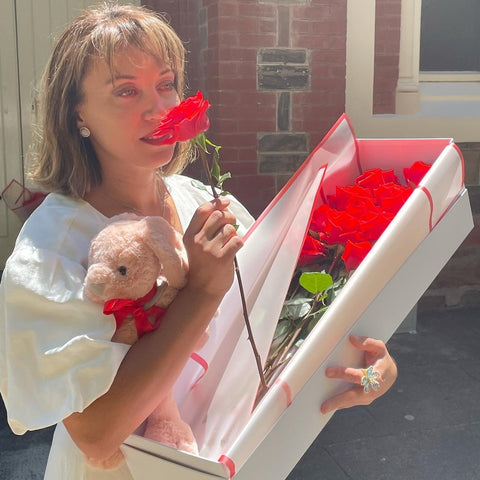 Savoring the joy of discovery, she holds the plush bunny close, with the Dozen Ferrari Red Roses box open before her, a moment treasured and made possible by Floral Atelier Australia, Adelaide's premier choice for heartfelt expressions and same day flower delivery