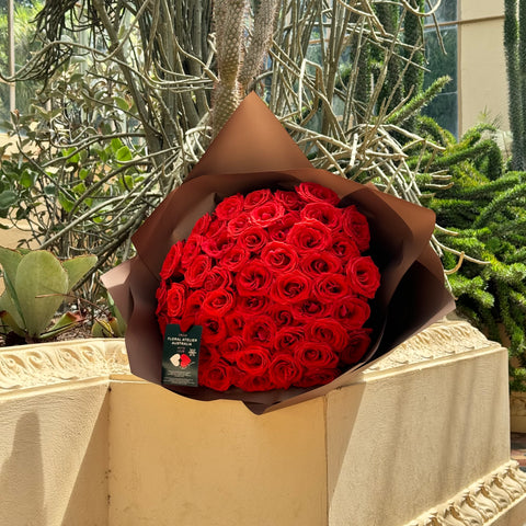 Floral Atelier Australia's Elegant 50 Ferrari Red Roses Bouquet stands out with its vibrant color against a backdrop of serene cacti, embodying Adelaide's unique natural beauty, ready for same day flower delivery.