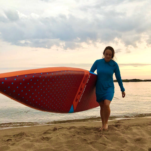Young woman carries her inflatable Stand Up Paddle Board across a Lake Superior Beach