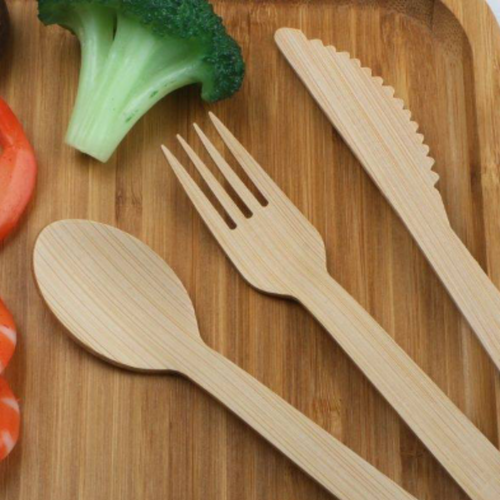 Bamboo cutlery set on next to brocolli on a cutting board