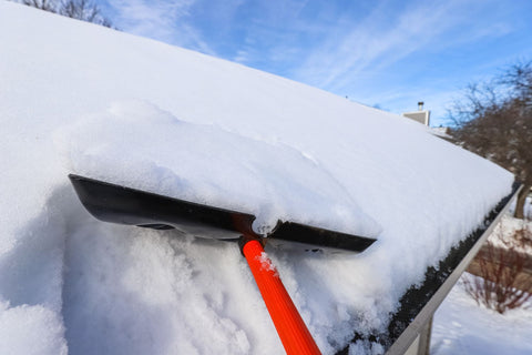 black shovel with red handle used to scoop heavy snow off of a roof in preventing ice dam formation