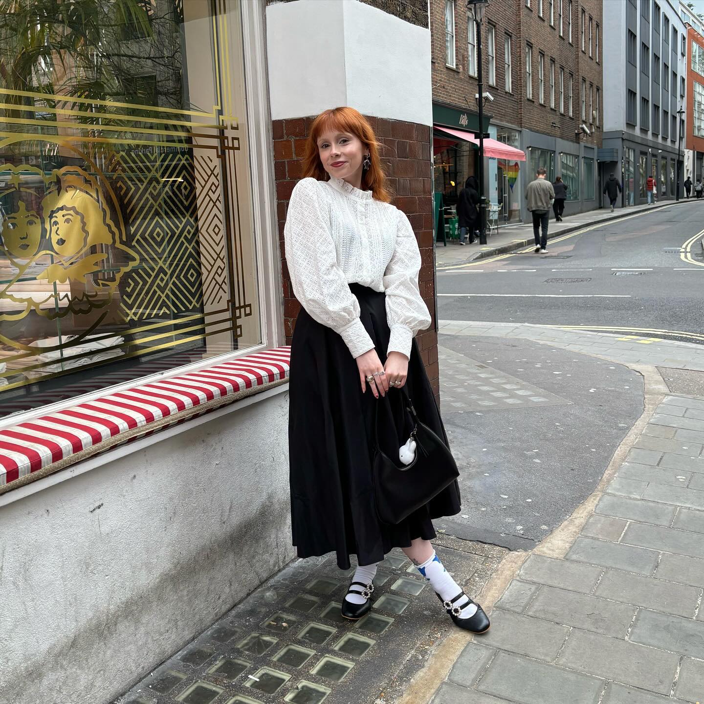 Content creator @alrstockwell in a black pleated maxi skirt and a white blouse posing in front of a window display