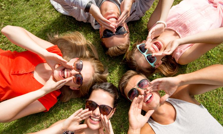 group lie on backs on grass looking up at camera with big healthy smiles