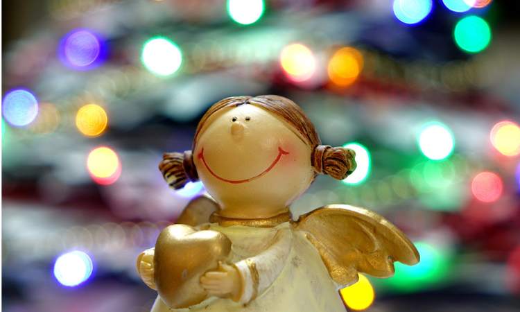 smiling cute Christmas angel doll with blurred coloured Christmas lights background