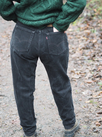 A woman stands with her back to camera wearing a pair of black Levis 550s and a green aran sweater