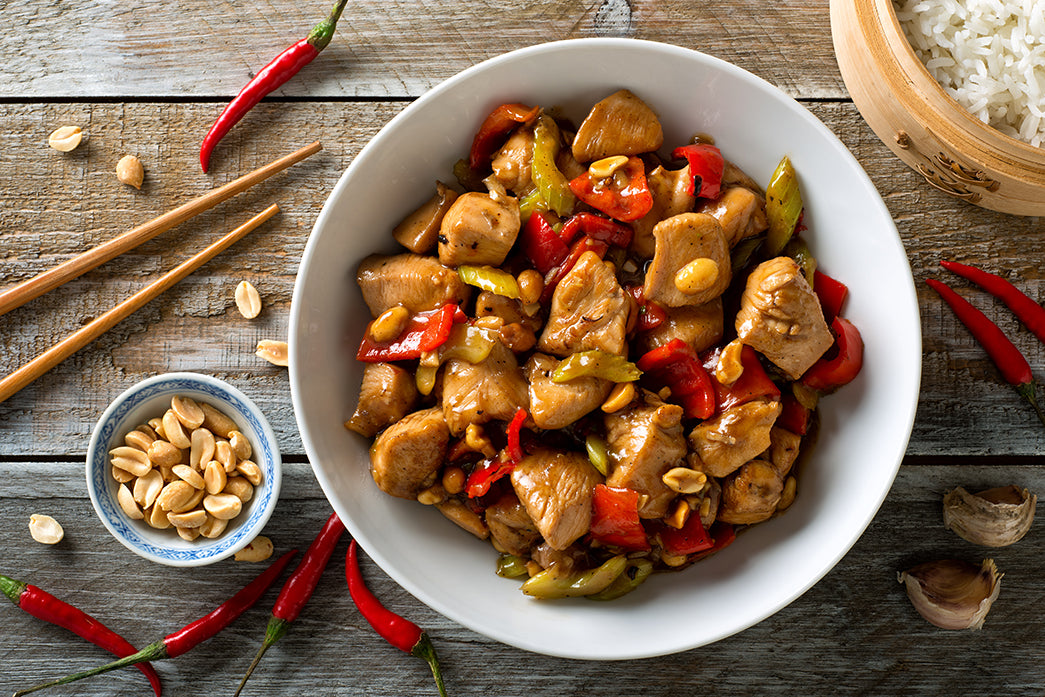 Kung Pao chicken in a white bowl with chopsticks and a bowl of peanuts