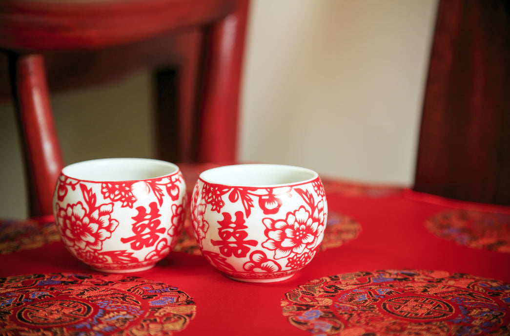 red tablecloth with two red and white cups, decorated with design and Chinese symbols for double happiness, with a red chair
