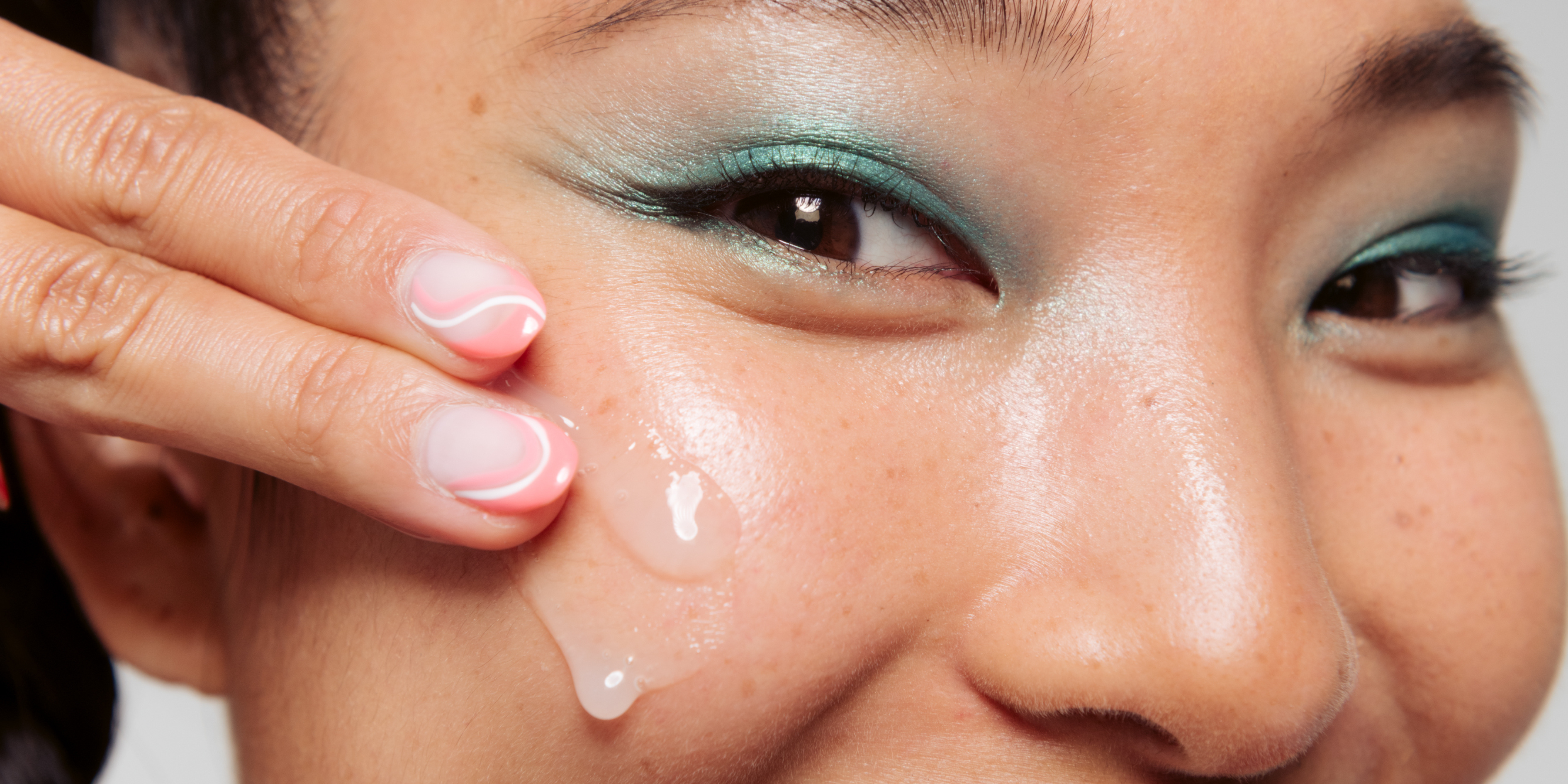 girl with blue eyeshadow, smiling, applying rebound serum to her cheek, tbh skincare, rosacea