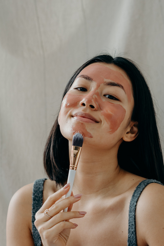 asian woman applying red clay mask