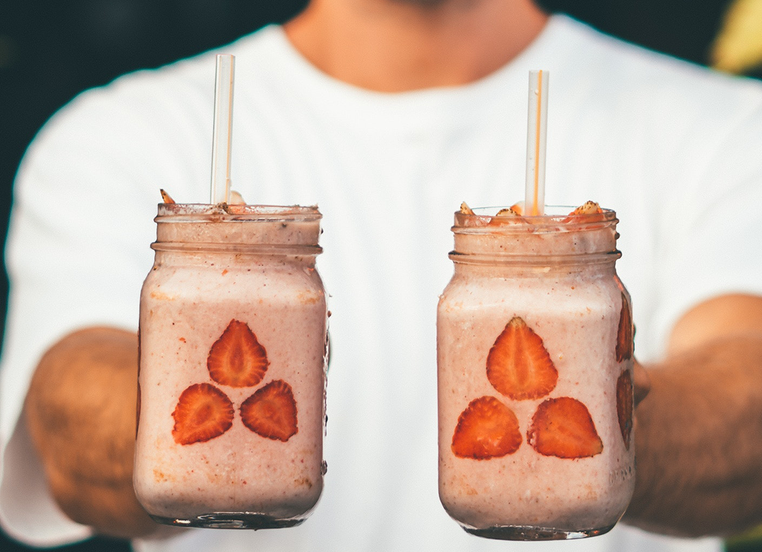 hands holding two smoothies with strawberries and sunbutter