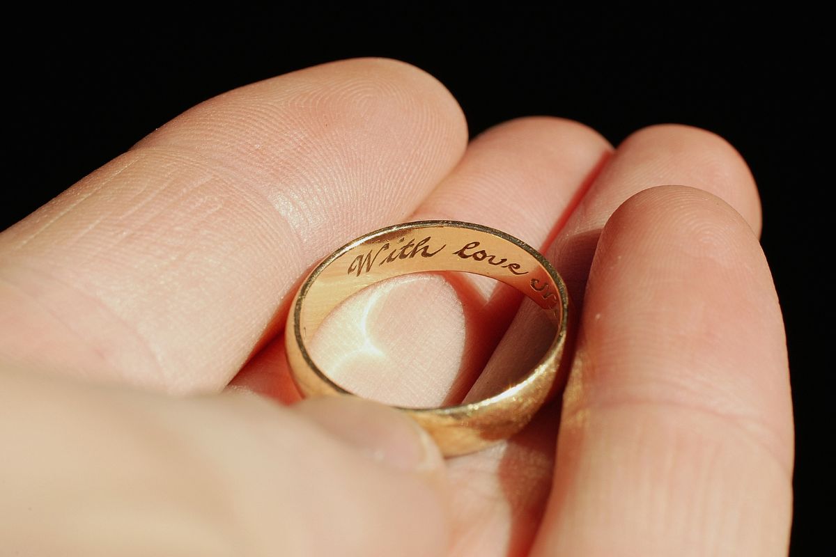 A man holds a wedding ring engraved with love